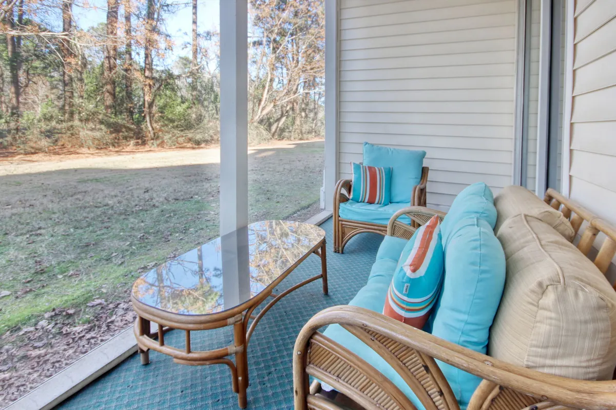 A cozy exterior porch with rattan seating, colorful cushions, a glass coffee table, and sturdy wooden columns. The seating area provides a comfortable spot to relax and enjoy views of the surrounding greenery, evoking the leisure and ease associated with golf resort living.