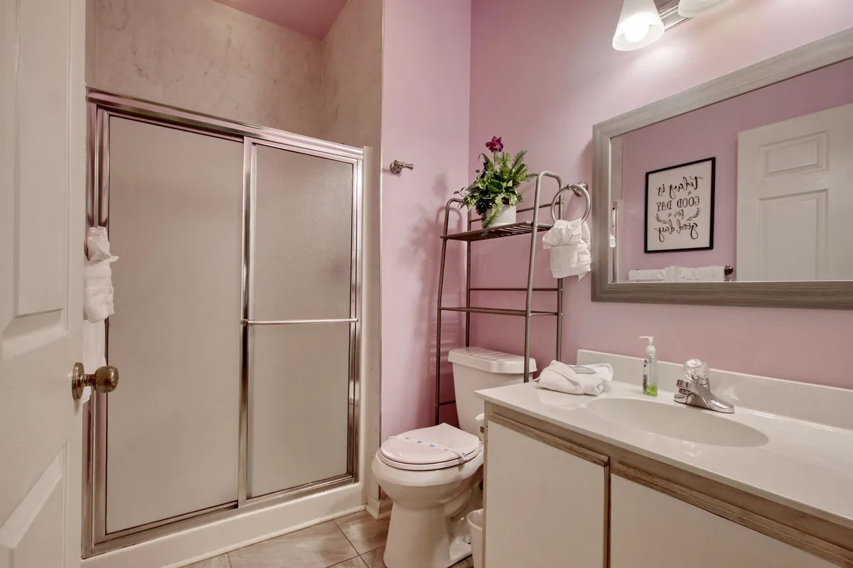 This clean and modern bathroom features a walk-in shower stall, vanity with sink, framed mirror, decorative plant, and toilet. The space is bright and organized, promoting a feeling of freshness and relaxation.