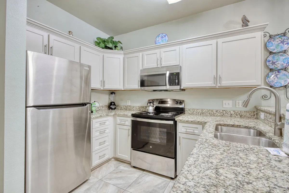 A welcoming kitchen view featuring a stainless steel refrigerator, granite countertop, small appliances, and decorative plates along the walls. The scene is set up for both cooking and enjoying morning coffee or a casual meal.
