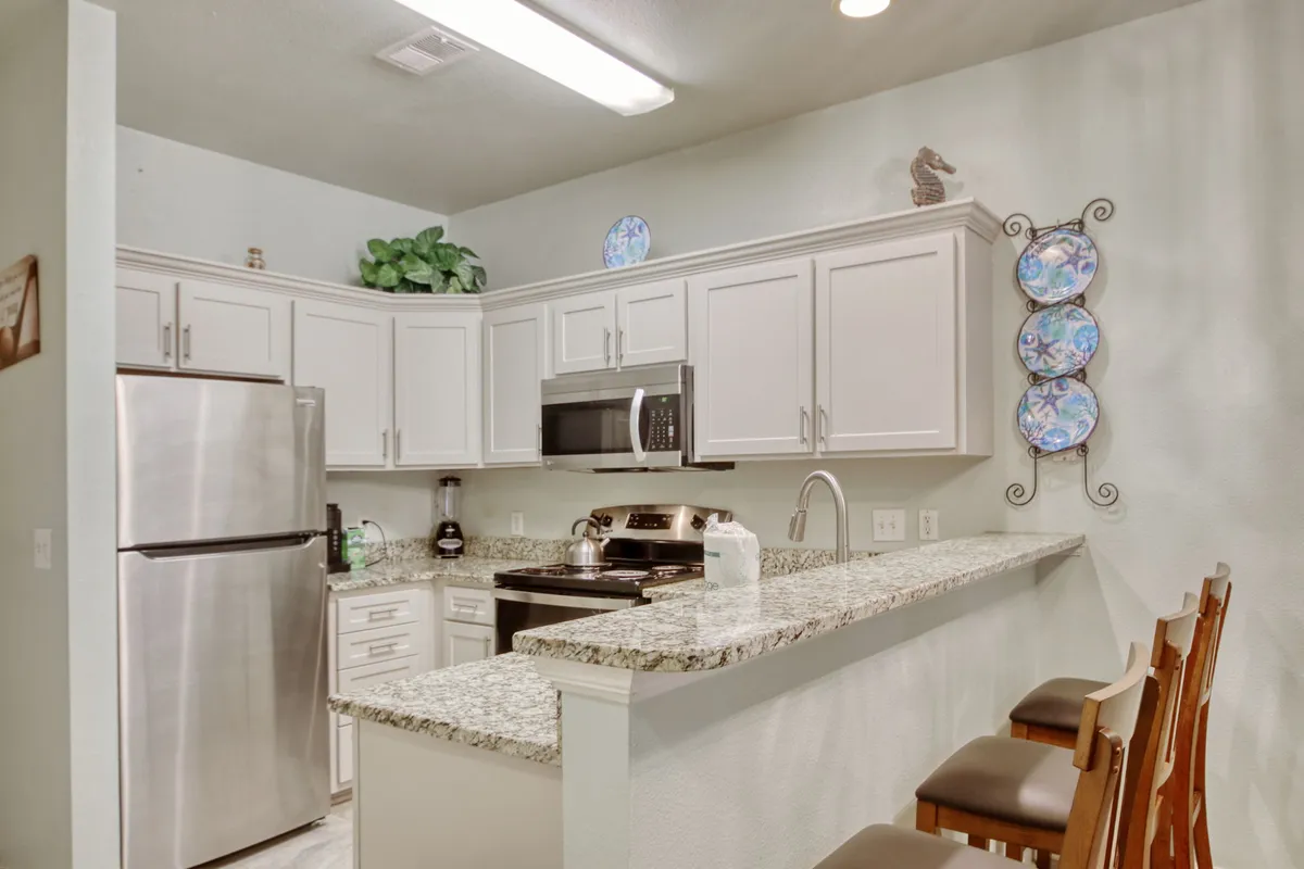 A warm kitchen scene with granite countertops, stainless steel appliances, decorative wall plates, and comfortable bar stools at the counter, creating a social space for cooking, baking, or enjoying a casual breakfast.