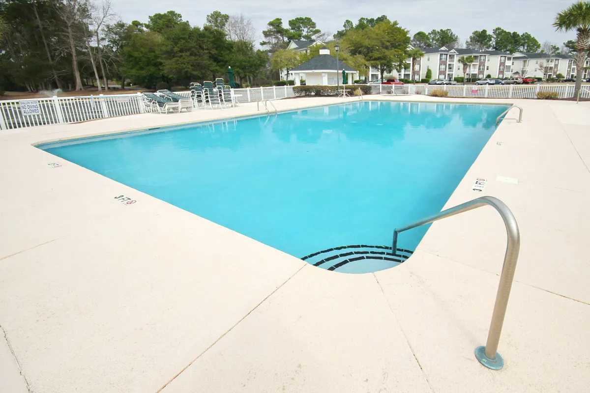 An inviting outdoor pool area surrounded by lush greenery, with lounge chairs arranged for relaxation and socializing. The water shimmers, and the area is bathed in sunlight, creating a vibrant, fun atmosphere ideal for families.