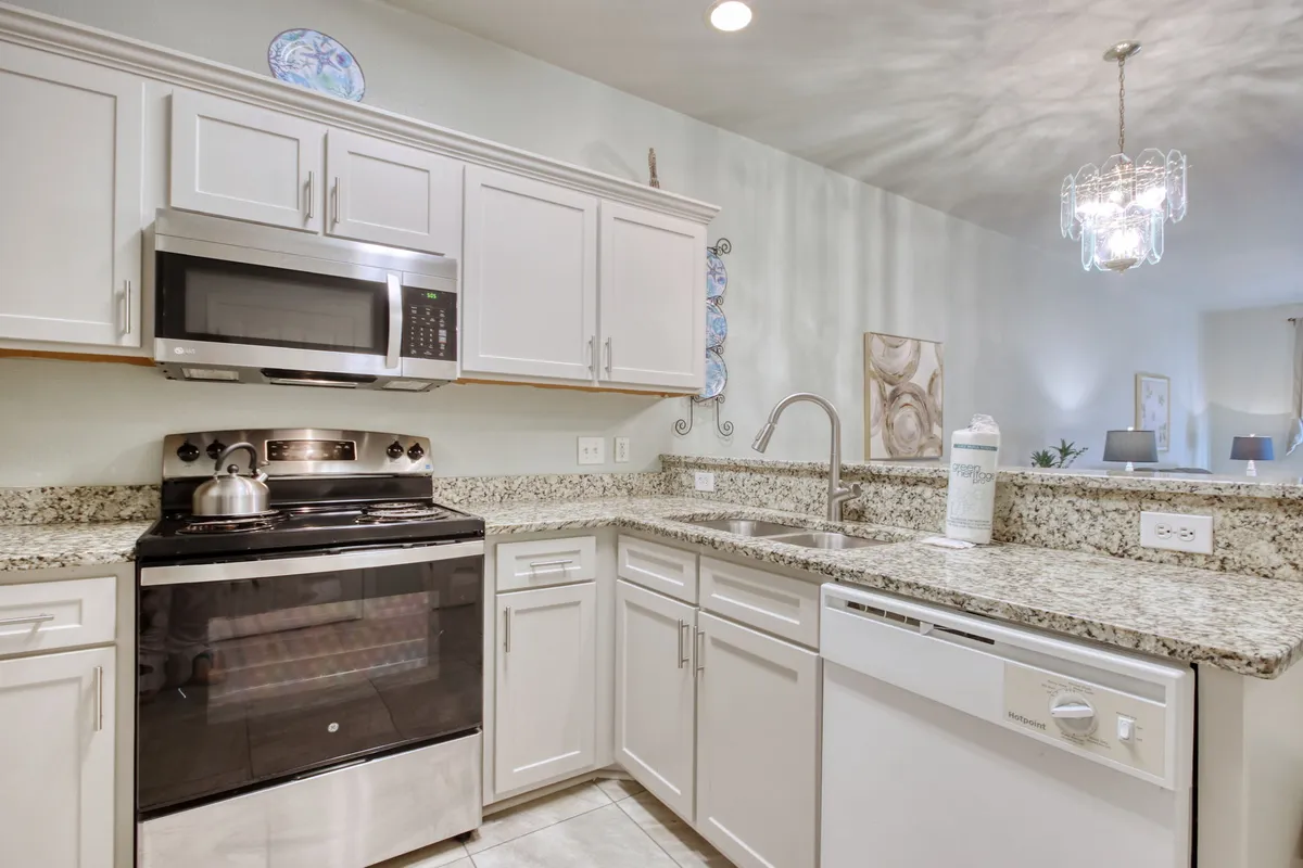 This image features a spacious kitchen with stainless steel appliances, elegant granite countertops, and a stylish chandelier overhead. The layout is open and inviting, with ample space for cooking, entertaining, and family gatherings.
