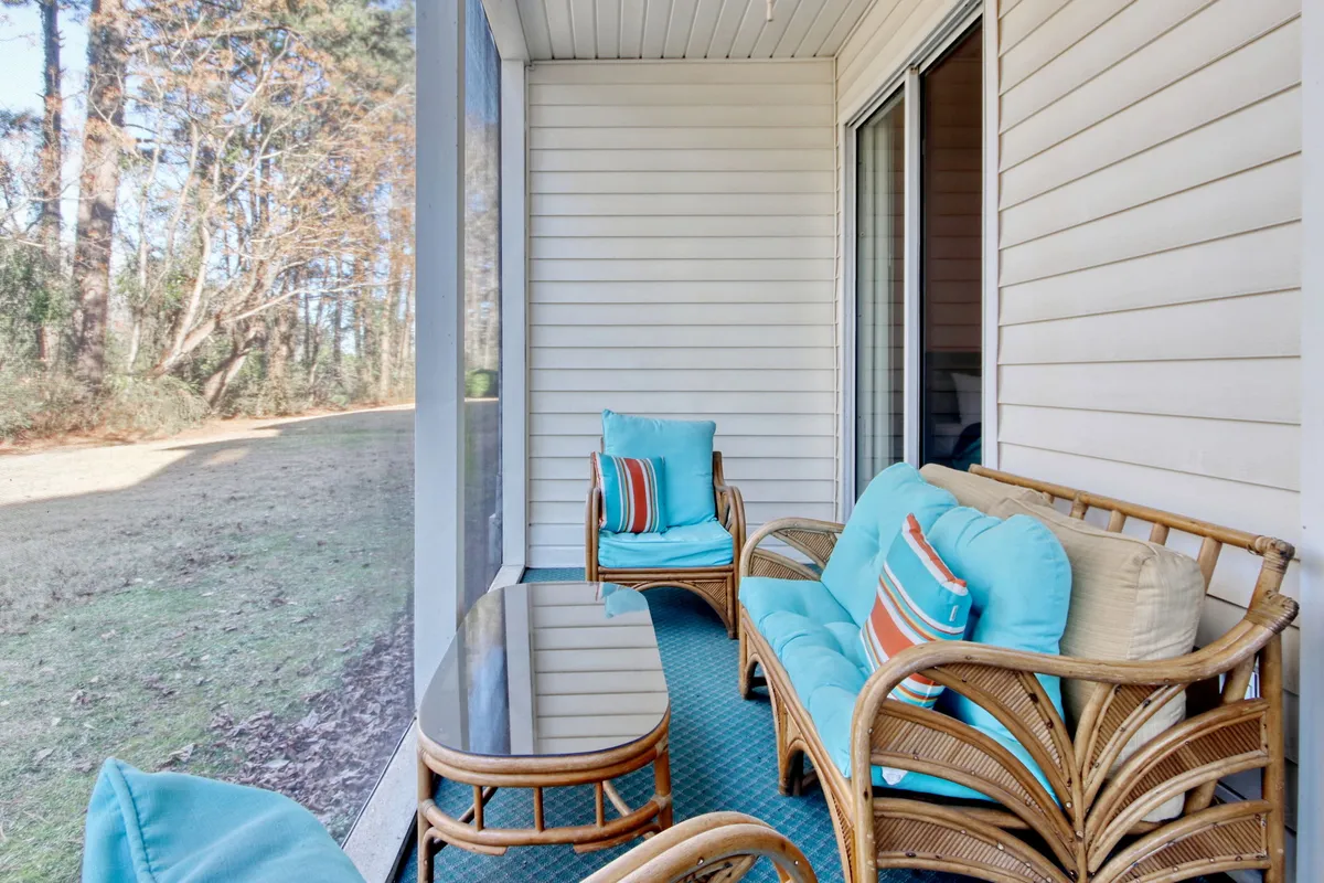 A tranquil interior space featuring rattan furniture with colorful cushions, positioned to take advantage of a view outside. The arrangement suggests a comfortable and inviting balcony or sunroom, perfect for enjoying a morning coffee or unwinding with friends. Soft natural light enhances the relaxing mood.