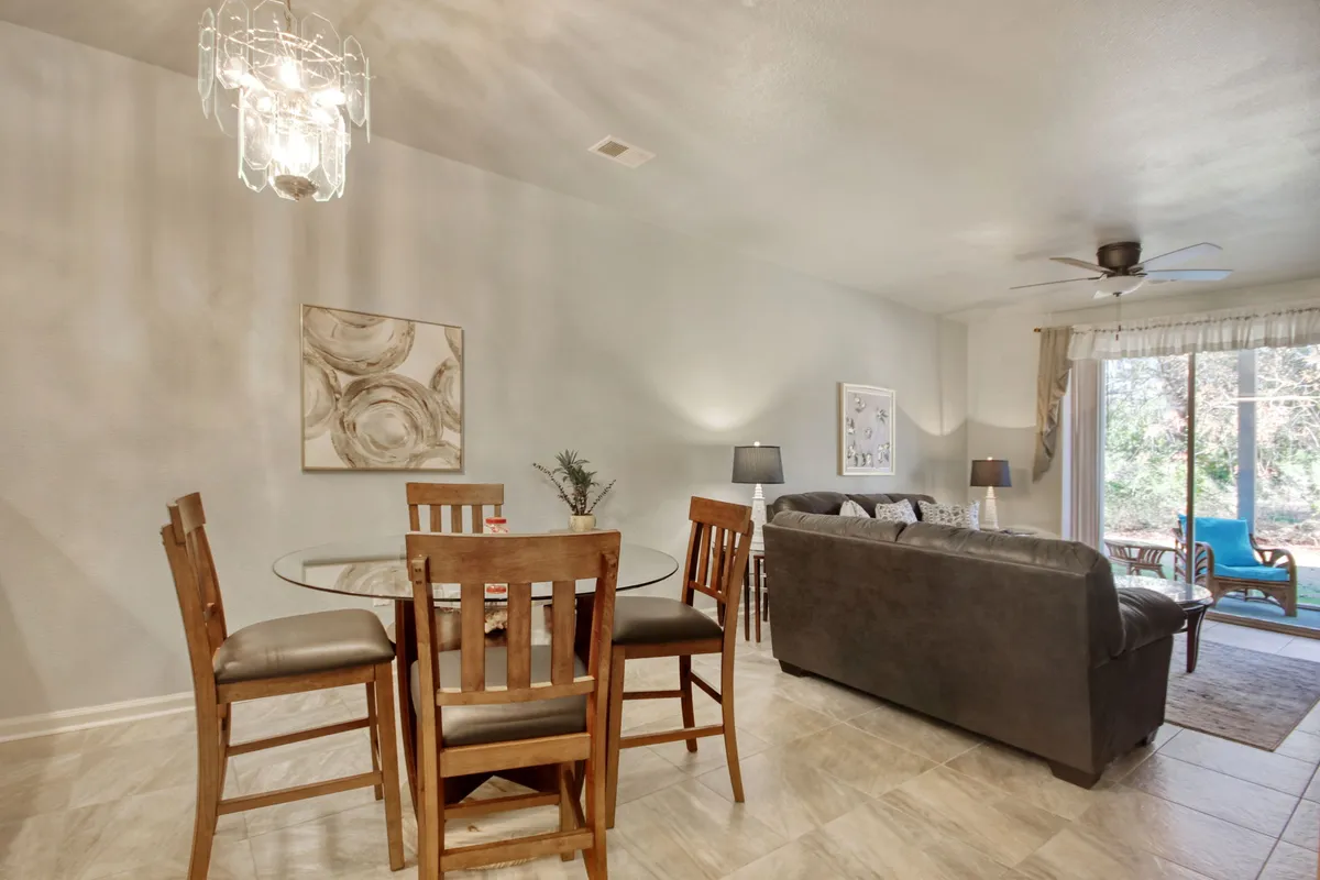 A flexible living and dining space featuring a round glass dining table and a brown leather sofa. Large sliding glass doors bathe the room in natural light and provide a view outdoors. Artwork on the wall and the seamless connection between spaces encourage gatherings and relaxation.